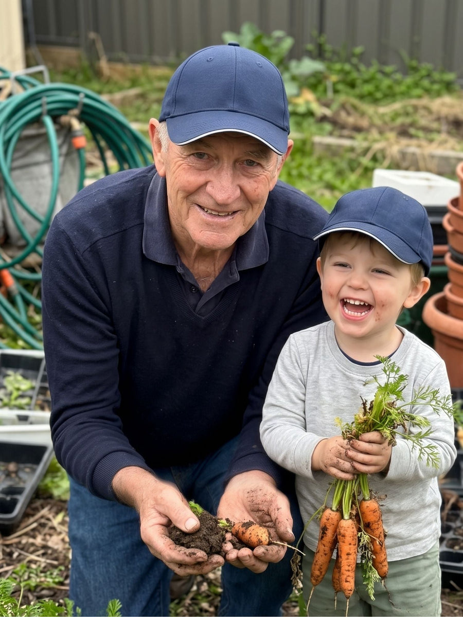 Navy — grandfather and grandson in matching navy Kindred Caps holding freshly pulled carrots in the garden