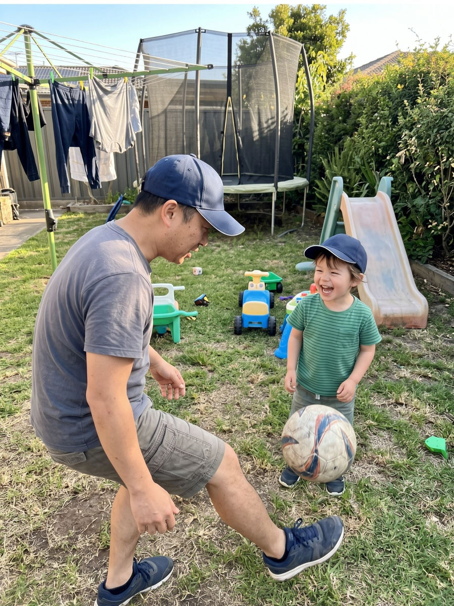 Navy — father and toddler in matching navy Kindred Caps playing soccer in the backyard