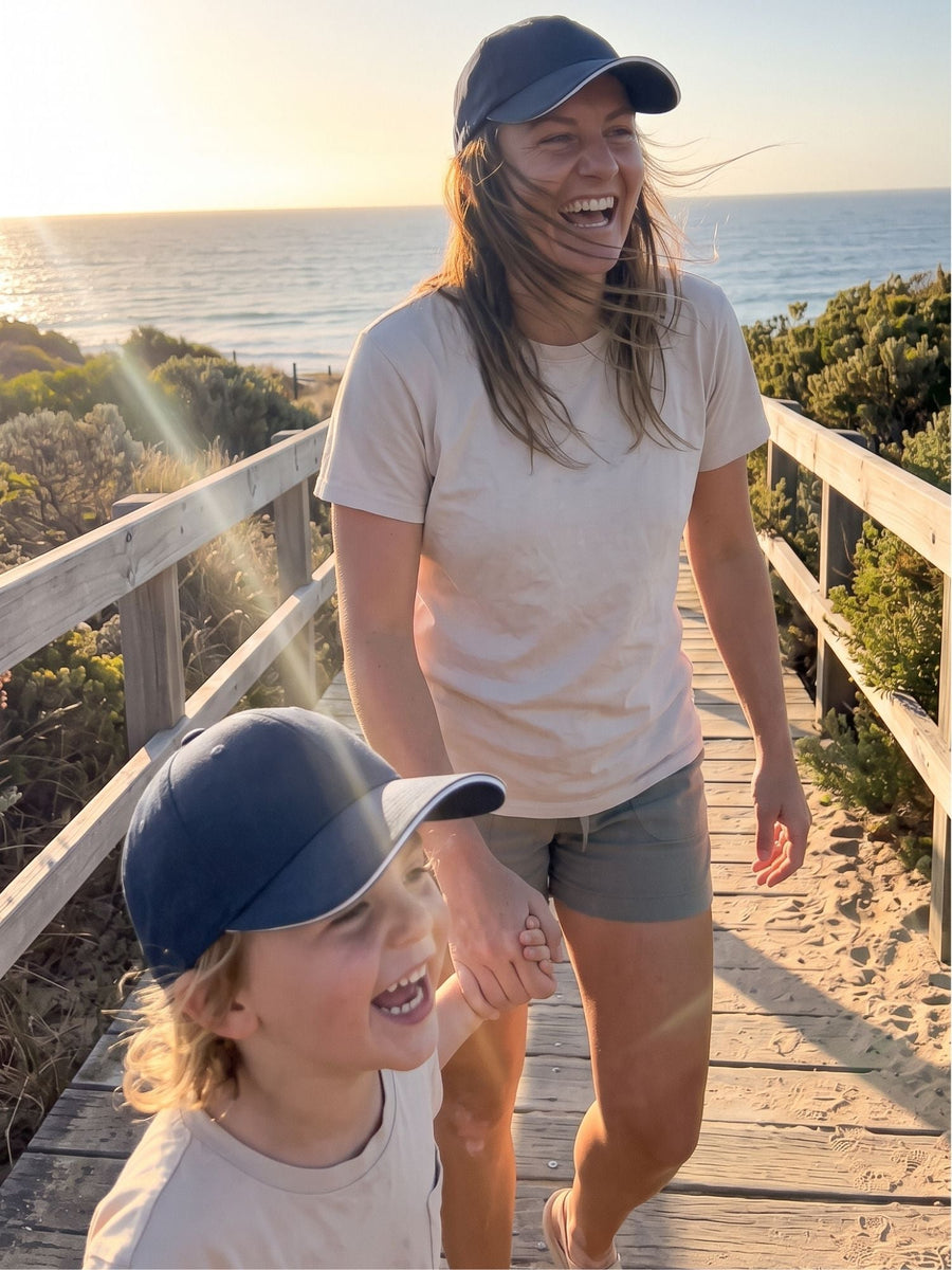 Navy — mother and child in matching navy Kindred Caps on a beach boardwalk at sunset